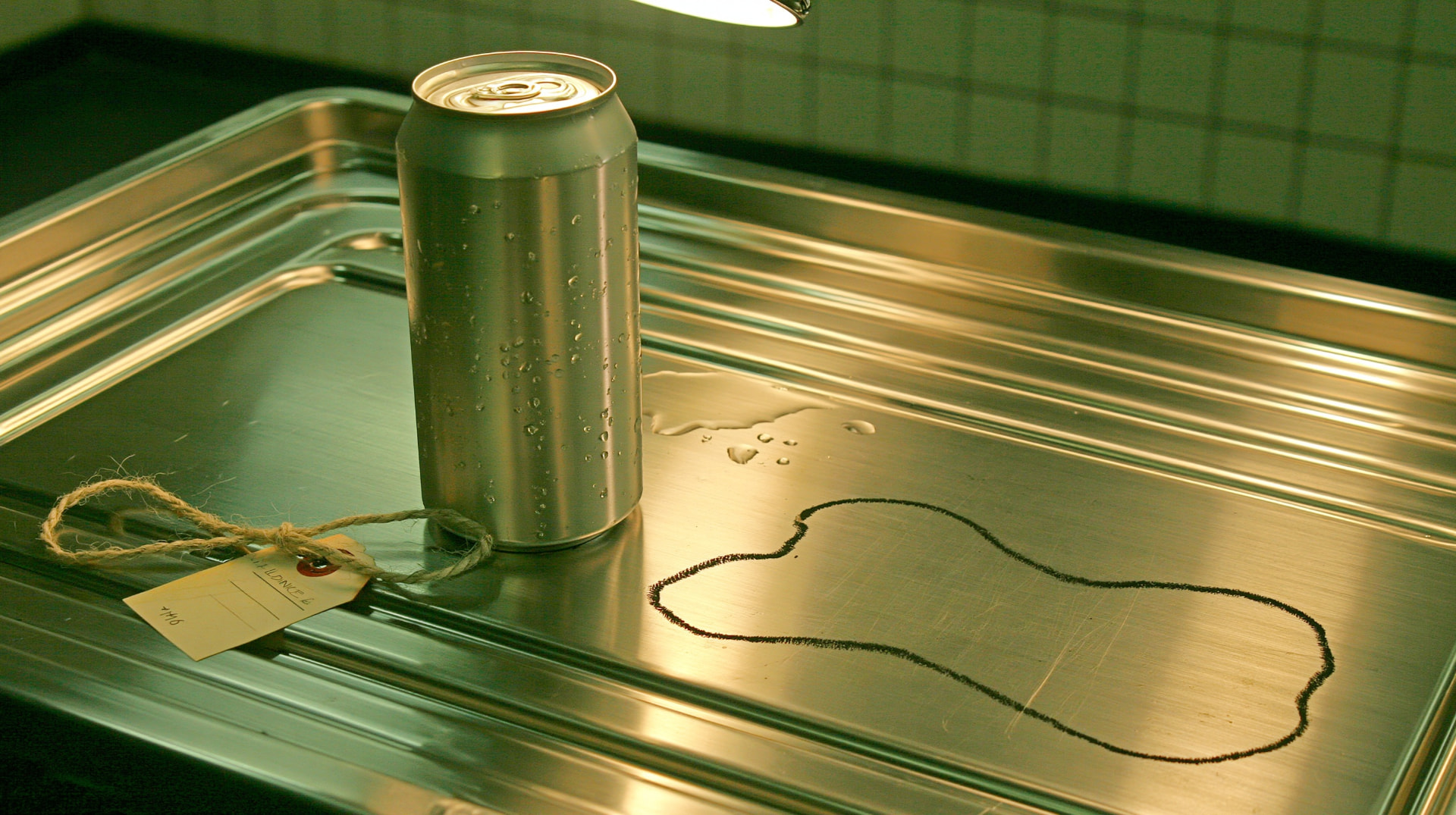 An unlabeled aluminum can on a steel autopsy table beside a chalk outline of a peanut.